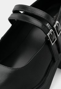 Μαύρο δερμάτινο παπούτσι Mary Jane με διπλές λουράκια και ασημένιες αγκράφες, με χαμηλό τακούνι και λεία επιφάνεια.