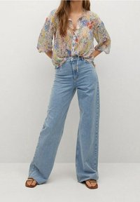 Blumenmuster Bluse aus transparentem Stoff mit kurzen Ärmeln und Knopfleiste, kombiniert mit hoch taillierten, hellblauen Schlagjeans und braunen Flip-Flops.