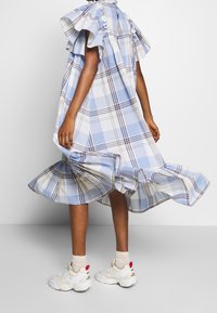 Modré kárované šaty s volánovými rukávy, rozšířeným lemem a knoflíkovými detaily. Nošeny s bílými teniskami s červeným detailem na zadní straně.