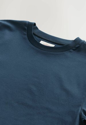 T-shirt en coton bleu marine à col rond, avec une texture lisse, des manches courtes et une étiquette cousue au niveau du col. Conception simple et décontractée.