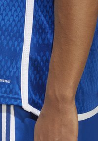 Maglia sportiva blu con un motivo a trama, rifiniture bianche e tessuto traspirante. Include il logo bianco in basso a sinistra.