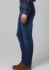 Pantalones vaqueros de mezclilla azul oscuro con corte recto, que cuentan con cinco bolsillos y detalles de costura sutiles. Combina con botas de tacón bajo de ante marrón.