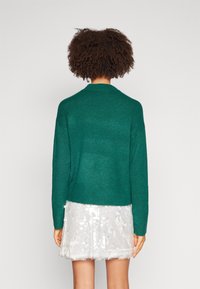 Groen gebreide trui met een ronde hals en geribbelde manchetten. Gecombineerd met een glanzende, met pailletten versierde witte rok.