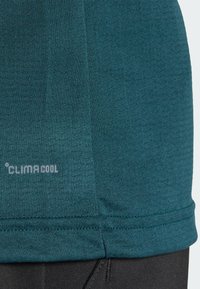 Turkusowa koszulka sportowa z teksturowanej tkaniny, z przeszyciem wzdłuż dołu i brandingiem CLIMACOOL, zaprojektowana z myślą o zarządzaniu wilgocią.
