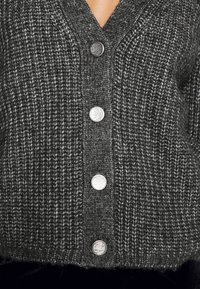 Šedý pletený cardigan s výstřihem do V, pěti stříbrnými knoflíky a texturovaným vzorem. Materiál vypadá měkce s útulným povrchem.