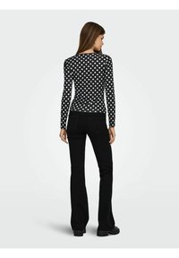 Schwarzes Langarmtop mit weißen Punkten, kombiniert mit schwarzen Schlagjeans. Hat einen runden Ausschnitt und eine figurbetonte Silhouette.