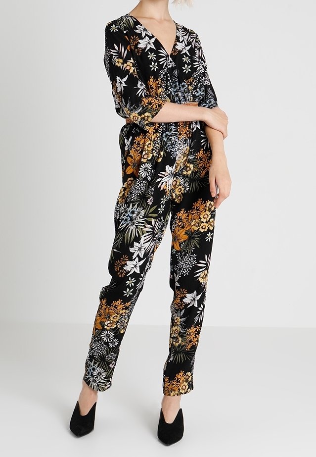 Tuta floreale con sfondo nero, caratterizzata da motivi arancioni, bianchi e verdi, scollatura a V e gambe affusolate. Tessuto morbido con una vestibilità comoda.