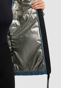Tessuto esterno nero con un rivestimento metallizzato argentato lucido. Accenti blu lungo la cucitura e un cursore della zip con dettagli testuali visibili.