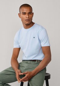 Svetlomodré tričko zo zmesi bavlny s krátkym rukávom, s malým tmavomodrým logom. Kombinované so zelenými nohavicami a tkaným opaskom.