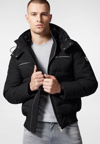 Czarna kurtka puchowa z odpinanym kapturem, z metalowymi suwakami, zamknięciem na zamek z przodu i kieszeniami bocznymi. Nosi się na szarej koszulce.