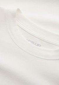 Weißes Baumwoll-T-Shirt mit Rundhalsausschnitt, das eine glatte Textur aufweist und ein dezentes „LEVELUP“-Label in Hellgrau am Innenkragen trägt.