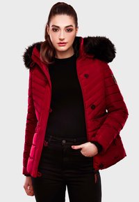 Red insulated jacket with a fur-lined hood, quilted texture, button closures, and adjustable drawstrings. Black top and pants worn underneath.