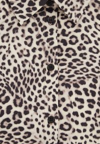 Tkanina s uzorkom leoparda s crnim dugmadima i ovratnikom na košulji, koja sadrži nepravilne crne mrlje na bež pozadini.