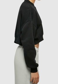 Felpa nera a maniche lunghe, con scollatura a girocollo, polsini a costine e texture morbida. Abbinata a pantaloni della tuta grigio chiaro.