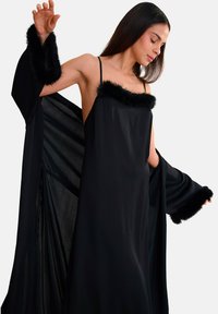 Robe noire à coupe ample, avec une douce bordure en fourrure noire au niveau de l'encolure et des manches. Fines bretelles et tissu fluide.