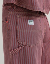 Rot- und marineblau gestrefter Stoff zeigt eine Gesäßtasche mit einem Logopatch. Merkmale sind sichtbare Nähte und ein seitliches Werkzeugtaschendesign.