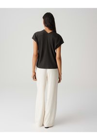 Top nero testurizzato con maniche corte, scollatura a V sul retro, indossato con pantaloni larghi crema. Design semplice, palette di colori neutri.