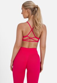 Top sportivo fucsia con design a incrocio, abbinato a leggings a vita alta coordinati. Tessuto morbido, materiale leggero.