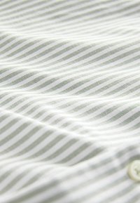 Tela a rayas verdes y blancas con una textura suave, que presenta rayas delgadas espaciadas uniformemente y un detalle de botón visible.