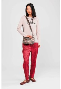 Top de manga larga en rosa pálido con escritura negra, pantalones de satén burdeos, planos marrones con tachuelas y un bolso cruzado estampado con correa de cadena.