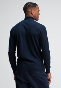 Marine gebreide trui met hoge kraag en textuurpatroon. Lange mouwen en geribbelde zoom verbeteren de pasvorm en het ontwerp.