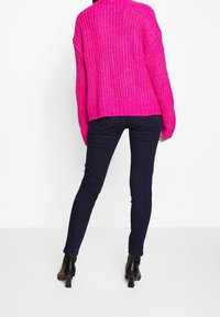 Suéter de punto rosa chicle difuso con corte holgado, combinado con jeans ajustados azul oscuro y botines de tacón negro.