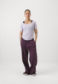 Haut à rayures léger violet avec des manches courtes et des détails en boutons, associé à un pantalon large violet foncé. Des baskets blanches complètent la tenue.