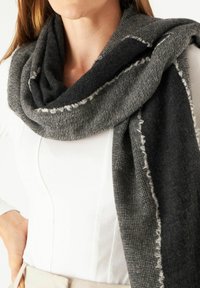 Écharpe noire et grise en tissu texturé avec des bords effilochés, enroulée autour du cou. L'écharpe a une section sombre unie et une section plus claire à motifs.