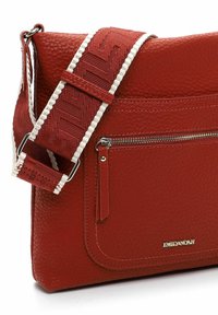 Red textured leather crossbody bag with a wide patterned strap, front zip pocket, and logo detail in a metallic finish.