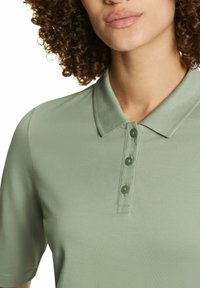 Lichtgroene polo met een gestructureerde stof, een klassieke kraag en drie knopen op de sluiting, met een eenvoudige en frisse uitstraling.