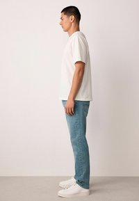 Hvid t-shirt med rund hals, lyseblå jeans og hvide sneakers. Simpelt design, tætsiddende pasform, med korte ærmer og rene linjer.