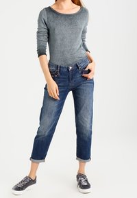 Grå långärmad topp, denimblå avslappnade jeans, uppvikt ärm, och grå sneakers. Slät tyg och avslappnad design med knäppning framtill.