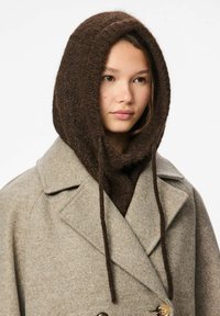 Sciarpa con cappuccio marrone in maglia testurizzata, indossata con un cappotto di lana grigio con design doppiopetto e grandi bottoni.