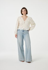 Witte geborduurde blouse met poffende mouwen, gekartelde zoom en knoopsluiting, gecombineerd met lichtblauwe wijde jeans.