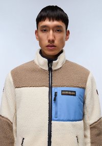 Fleecejakke med creme, beige og bl�å paneler, lynlåslommer, høj krave og logopatch på brystet. Blødt, struktureret materiale.