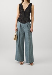 Sort broderet peplum top med dyb V-udskæring, parret med vide lyseblå bukser og beige blokhælede sandaler.