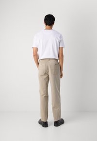Beige cotton pants with a straight leg fit, two back pockets, and a subtle texture. Worn with a plain white t-shirt and black shoes.