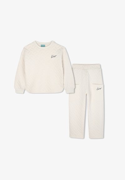 Haut à manches longues en tissu matelassé crème avec un pantalon assorti, doté de poignets côtelés et du logo Kenzo sur la poitrine et la poche, sur fond blanc.