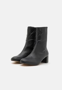 Botines negros de piel suave, con un tacón rectangular delgado y un diseño de punta afilada. Estilo minimalista sin herrajes visibles.