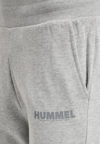 Grå mysbyxor gjorda av en bomullsmaterialblandning, med en ribbad midja, sidofickor och en grå logotryck på vänster lår.