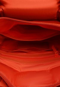 Roter gesteppter Handtascheninnenraum mit mehreren Fächern, darunter ein Reißverschlussfach und glatte Fütterung. Verfügt über einen Reißverschlussverschluss an der Oberseite.