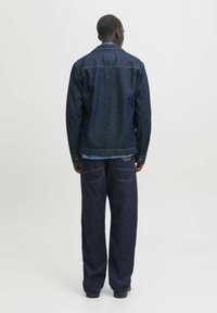 Chaqueta de mezclilla azul oscuro con un par coincidente de jeans de corte holgado. La chaqueta presenta un cuello con solapa y cierre de botones.