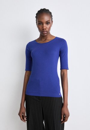 T-shirt à manches courtes, ajusté, en tissu tricoté bleu vif avec un col rond. Doté d'un petit logo près de l'ourlet. Associé à un pantalon à rayures.