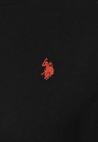 Black sweater with a textured fabric, featuring a small red embroidered logo depicting two figures. Round neckline, no additional patterns.