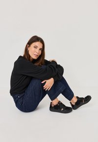 Black sweatshirt with long sleeves, dark denim wide-leg pants, and black sneakers featuring copper accents, sitting on a light background.