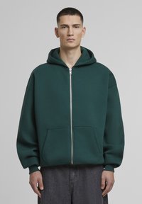 Grøn zip-up hoodie lavet af blødt stof, med en stor hætte, forlommer, ribbede manchetter og en afslappet pasform.