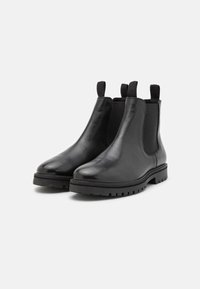 Par de botas Chelsea de cuero negro con paneles laterales elásticos y tiradores, con suelas de goma de patrón grueso.