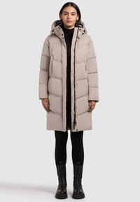 Gai smilškrāsas pūkains mētelis ar noņemamu kapuci, ar izšūtu dizainu, priekšējo rāvējslēdzēju, sānu kabatām un vidēja garuma griezumu. Melna adīta iekšējā drēbe.