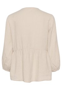 Beigenvärinen pellavapusero, jossa on pyöreä pääntie, pitkät pussihihat ja kerätty vyötärönauha. Kangas on hienovaraisesti teksturoitu ja laskeutuu pehmeästi.