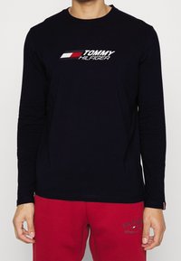 Laivastonsininen pitkähihaisen T-paita, joka on valmistettu puuvillasta ja jossa on valkoinen ja punainen "TOMMY HILFIGER" -logo rinnassa sekä pyöreä pääntie.